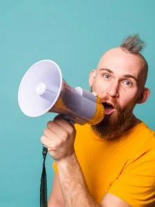 Bearded european man in yellow shirt isolated on turquoise background crazy shouting in megaphone loudspeaker, attention!